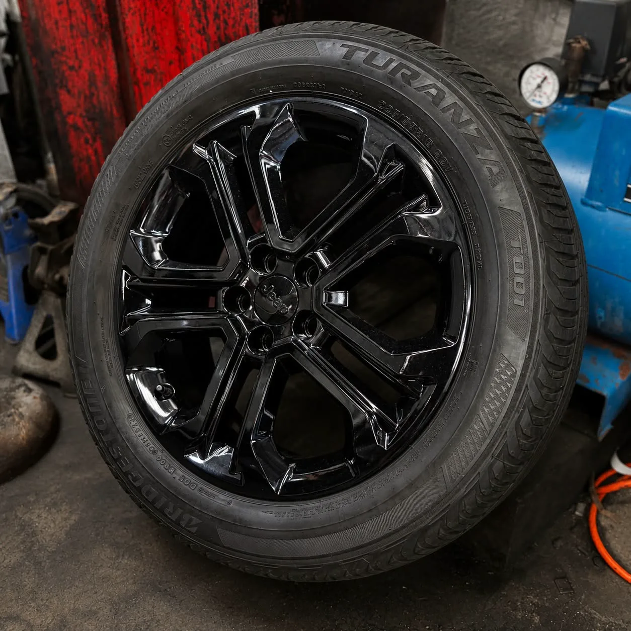 A black alloy wheel fitted with a Bridgestone Turanza tyre, resting in the workshop