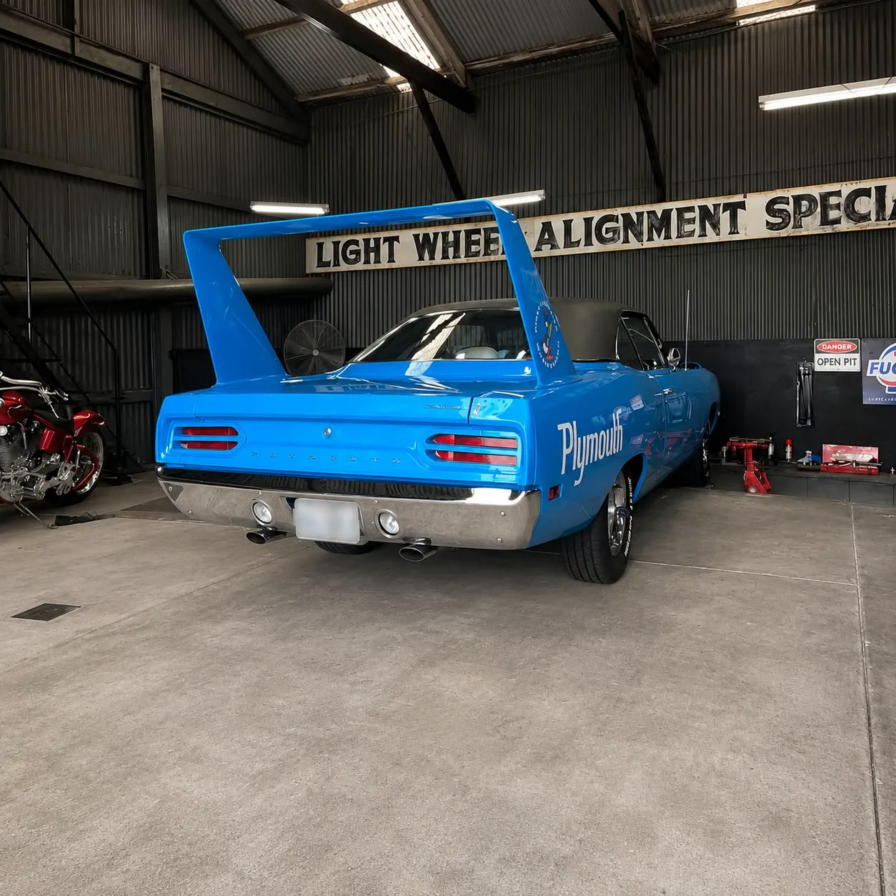 A blue classic muscle car parked beneath the workshop sign