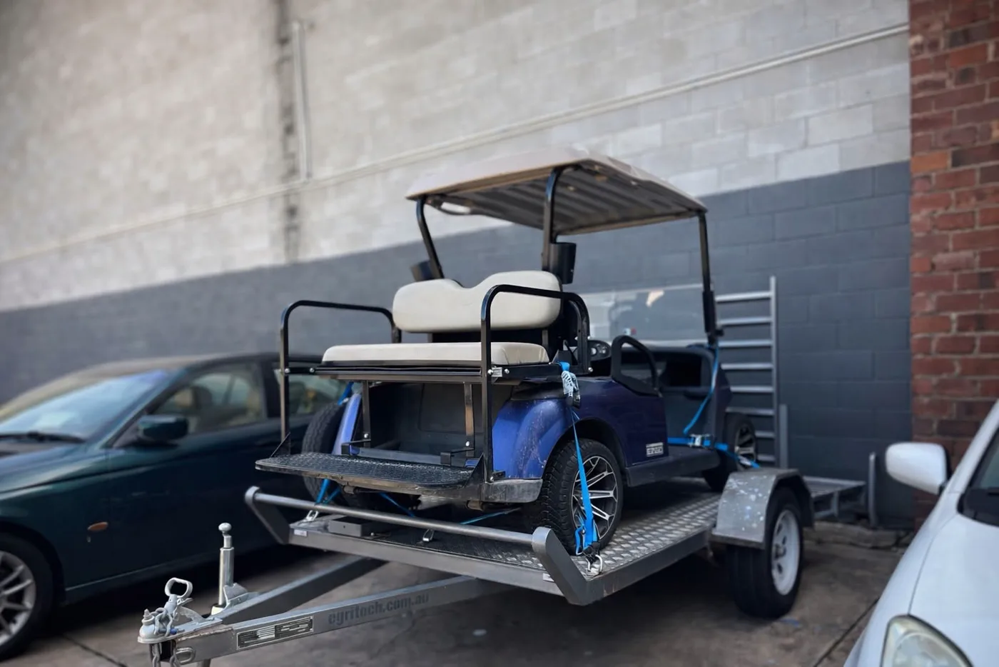 A golf buggy loaded on a trailer outside the workshop