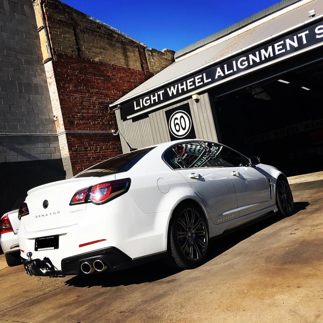 A white Holden Commodore parked outside the workshop beneath the Light Wheel Alignment Specialists entrance sign
