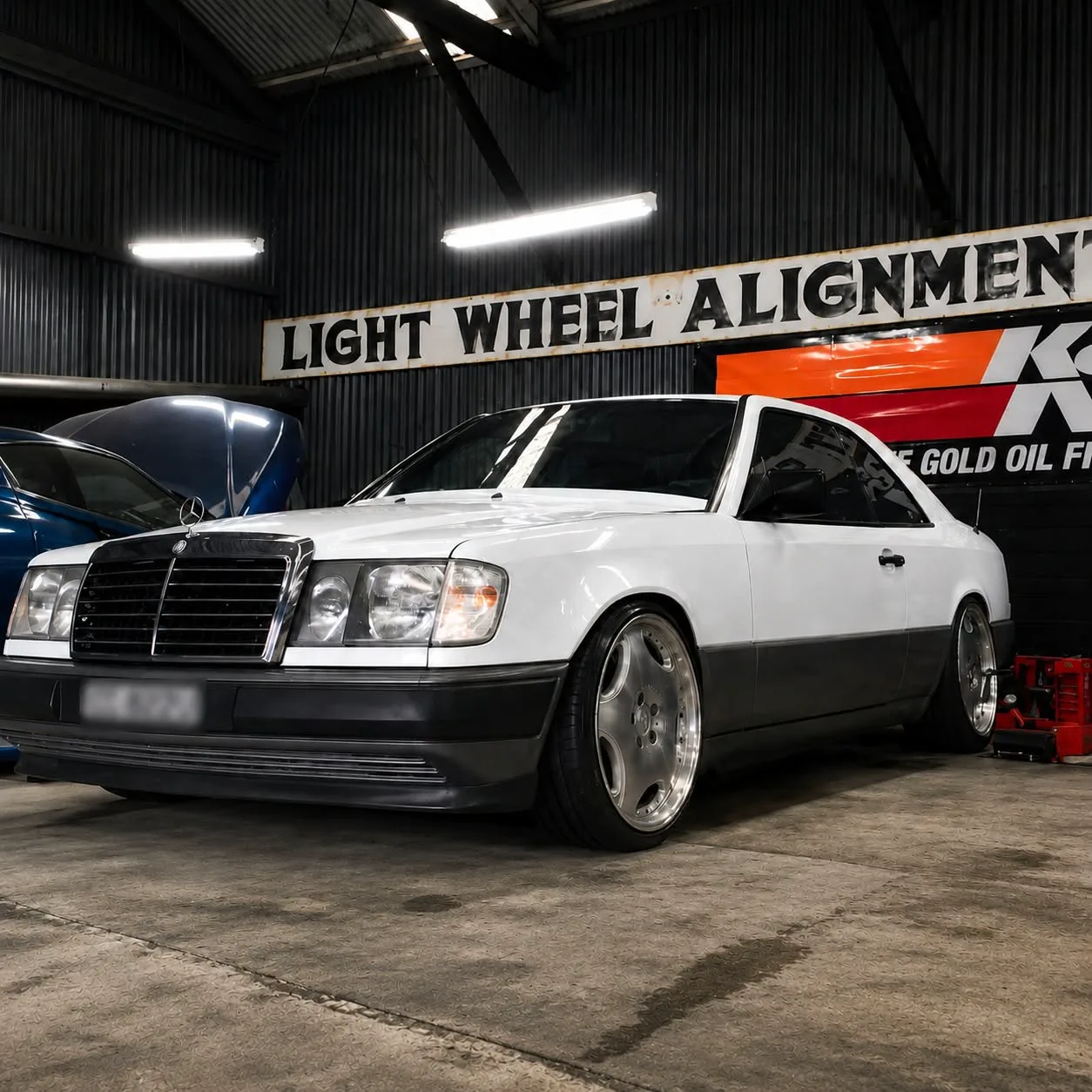 A white Mercedes-Benz coupe parked under the workshop sign