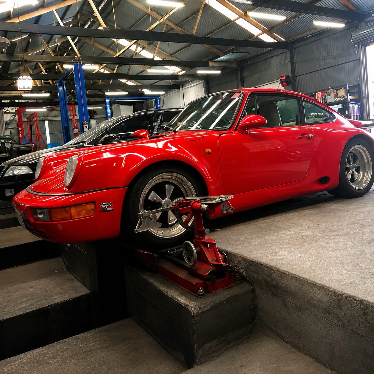 A silver Porsche 911 positioned over the wheel alignment pit inside the workshop