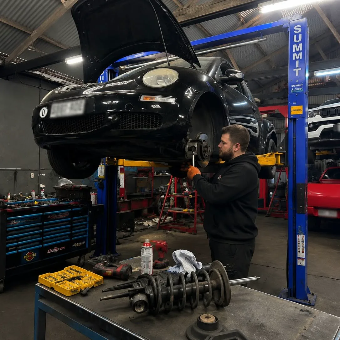 Suspension and driveline components laid out on the bench while a car sits raised on the workshop hoist
